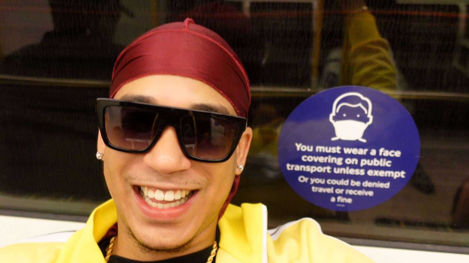 Joshua Arthur smiling on the London Underground beside a face-covering notice