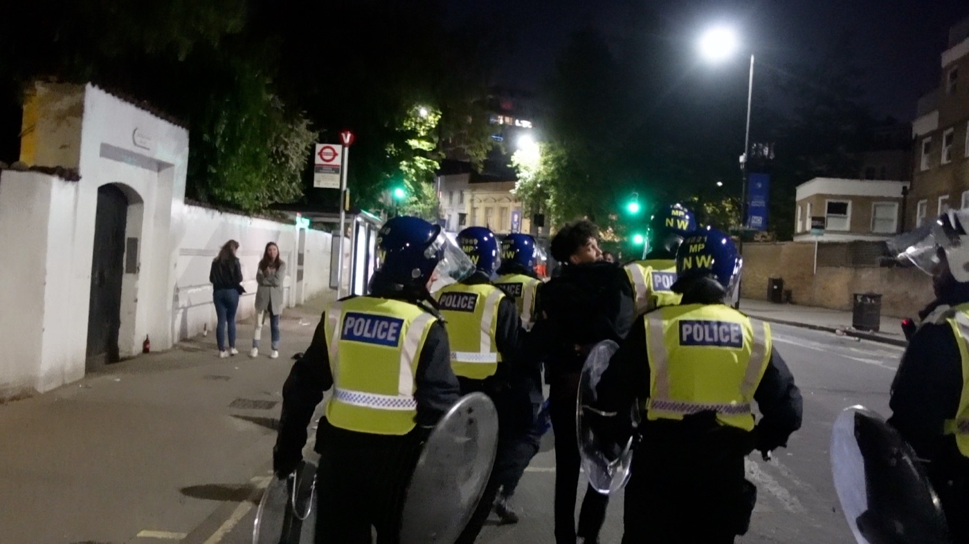 Joshua Arthur escorted along a street at night by Metropolitan Police officers in riot helmets, from the documentary Am I Really Free?