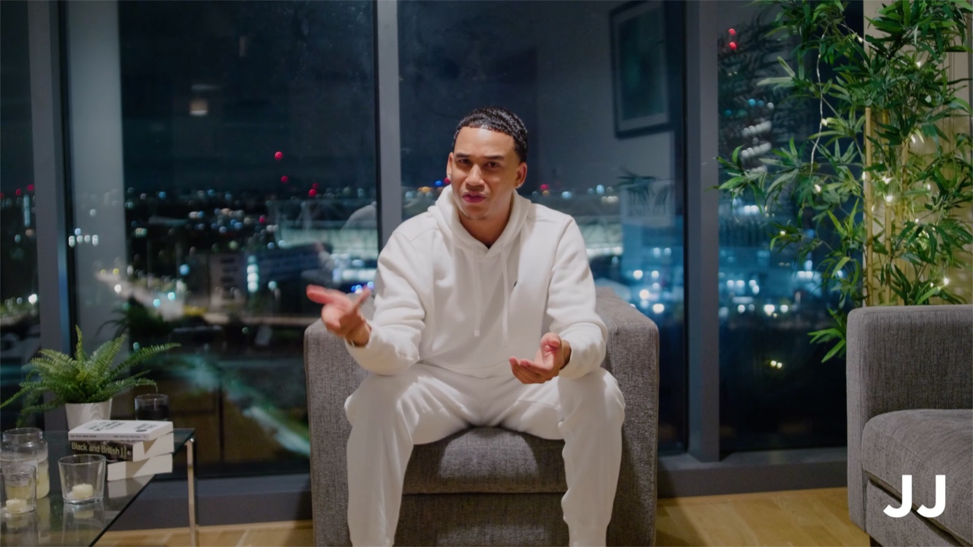 Joshua Arthur seated, speaking directly to camera against a night skyline, from the documentary Am I Really Free?
